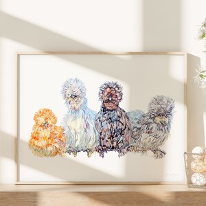 A print of four beautiful silkie chickens painted in watercolour. There are birds of four different colours sitting in a row. The print is framed in a bright kitchen next to a basket of eggs and daisy flowers.