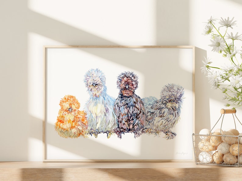 A print of four beautiful silkie chickens painted in watercolour. There are birds of four different colours sitting in a row. The print is framed in a bright kitchen next to a basket of eggs and daisy flowers.