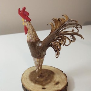 May include: A wooden rooster figurine with a red comb and wattle, brown and white feathers, and a brown wooden base.