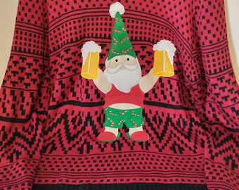 Op de afbeelding: Rode kersttrui met een zwart-wit geometrisch patroon en een cartoon kerstman ontwerp. De kerstman draagt een groene hoed en houdt twee bierpullen vast. De trui heeft een zwarte geribbelde zoom en manchetten.