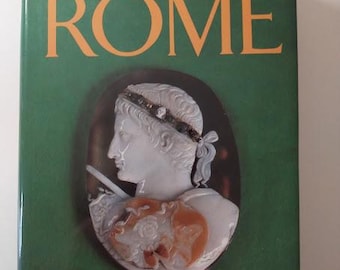 May include: A green book cover with the title "HISTORY OF ROME" in gold lettering. The cover features a cameo of a person's profile with a gold headband and a white background. The author's name, "Michael Grant", is printed in gold lettering at the bottom of the cover.