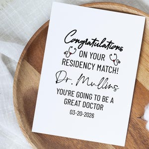 May include: A white card with black script congratulates on a residency match. The card includes the name "Dr. Mullins" and the date 03-20-2026. Two stethoscope graphics are also present.