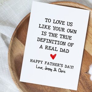 May include: A white card with black text that reads "To love us like your own is the true definition of a real dad. Happy Father's Day! Love, Jenny & Chris". A red heart is drawn above the text "Happy Father's Day!"