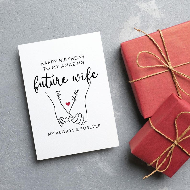 Może przedstawiać: Biała kartka z życzeniami z napisem "Happy Birthday to my amazing future wife" oraz imionami "Olivia" i "Justin" z czerwonym sercem. Dwa czerwone prezenty przewiązane sznurkiem znajdują się po prawej stronie.