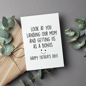 May include: A white card with black text that reads "LOOK AT YOU LANDING OUR MOM AND GETTING US AS A BONUS HAPPY FATHER'S DAY!" with a smiley face drawn below the text.