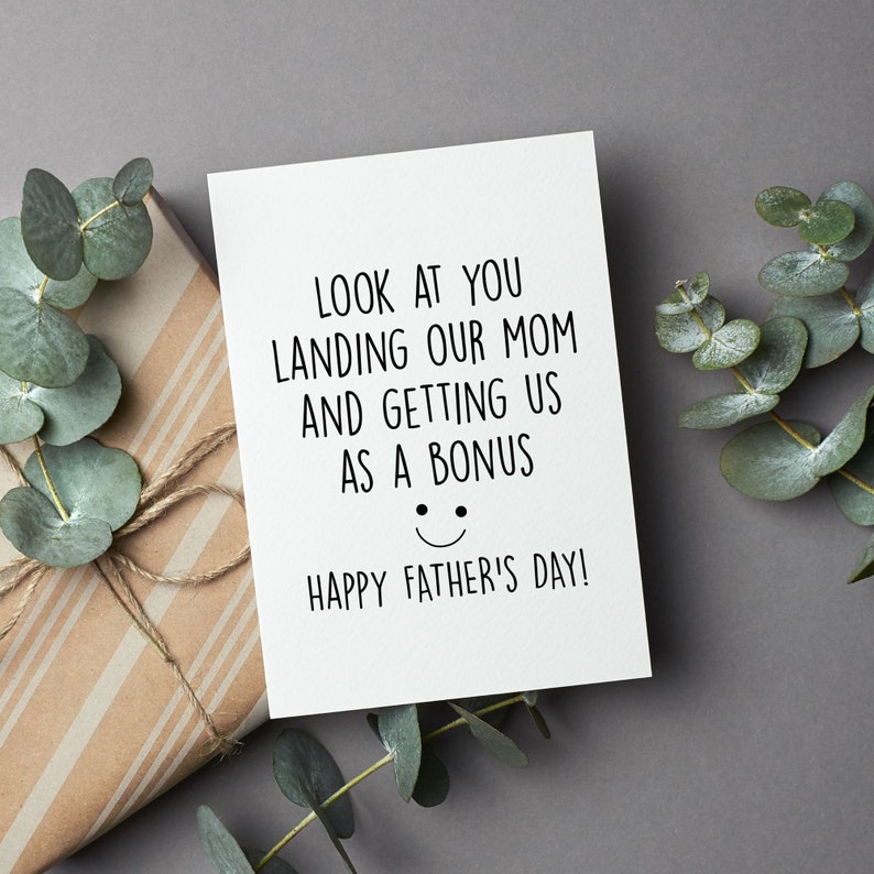 May include: A white card with black text that reads "LOOK AT YOU LANDING OUR MOM AND GETTING US AS A BONUS HAPPY FATHER'S DAY!" with a smiley face drawn below the text.