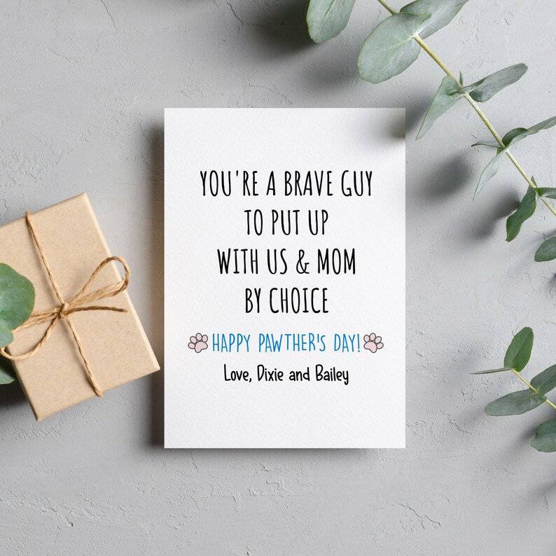 May include: A white greeting card with black text that reads "YOU'RE A BRAVE GUY TO PUT UP WITH US & MOM BY CHOICE." Below, in blue, it says "HAPPY PAWTHER'S DAY!" and "Love, Dixie and Bailey." A small gift box is on the left.
