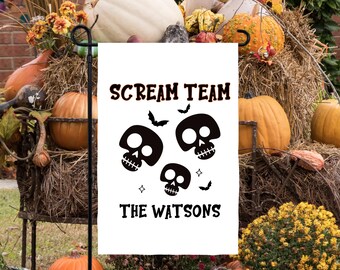 May include: A white Halloween garden flag with the text "SCREAM TEAM" above three black skull graphics and the text "THE WATSONS" below. The flag is displayed in a garden setting with pumpkins and hay.