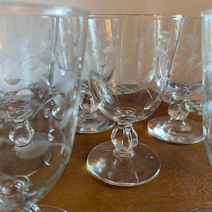 May include: Set of six clear glass wine glasses with etched floral designs. The glasses have a stemmed base and a round bowl.