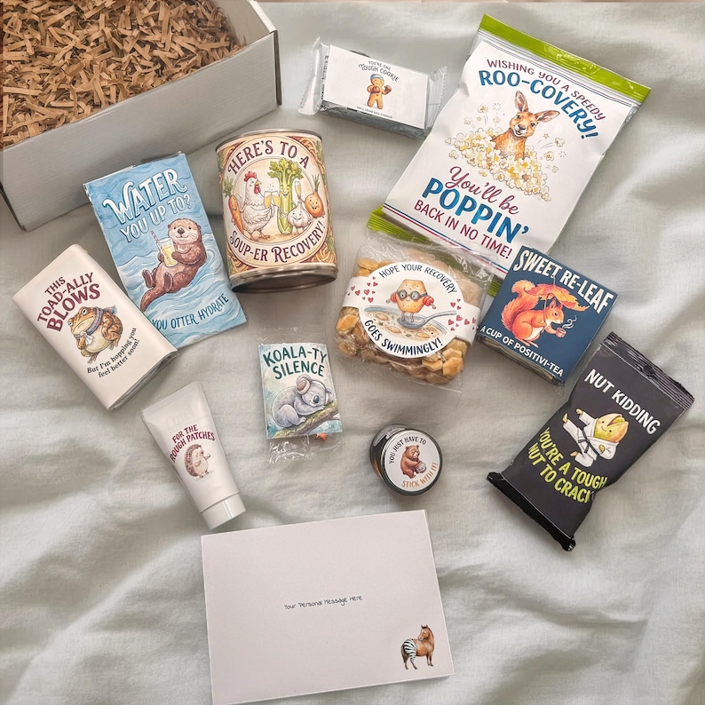 Flat lay of ankle recovery gift basket contents spread out on a white sheet. Includes soup, popcorn, cookies, tea, and comfort items, each applied with a custom sticker featuring a funny get well pun and cute illustration.