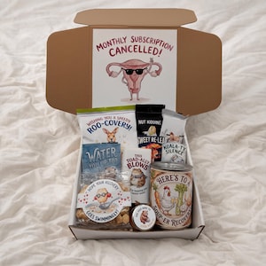 May include: A gift box with various recovery-themed items. The box includes snacks, a can of soup, and a card that reads "Monthly Subscription Cancelled!" with a cartoon uterus. Other items include a bag of chips with a kangaroo, and a small jar.
