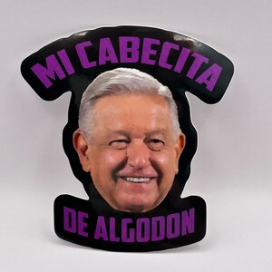 May include: A black and white sticker with a purple text overlay. The text reads "Mi Cabecita De Algodon". The sticker features a cartoon image of a man's face.