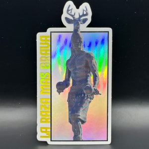 May include: A holographic sticker with a colorful background and a black and white image of a person with a deer head. The text "LA RAZA MAS BRAVA" is written vertically on the left side of the sticker.