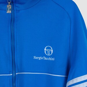 May include: A blue zip-up jacket with white stripes on the sleeves and a white Sergio Tacchini logo on the chest.