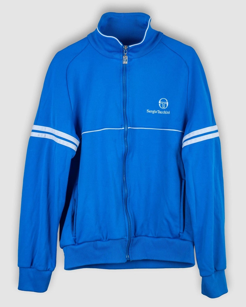 May include: A blue zip-up jacket with white stripes on the sleeves and a white Sergio Tacchini logo on the chest.