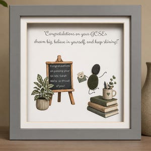 May include: A framed pebble art piece featuring a chalkboard with the text Congratulations on passing your GCSEs Sarah We're so Proud of you! and Congratulations on your GCSEs dream big, believe in yourself, and keep shining! with a pebble figure.