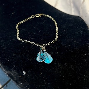 May include: A gold chain bracelet with a charm of two blue feathers.