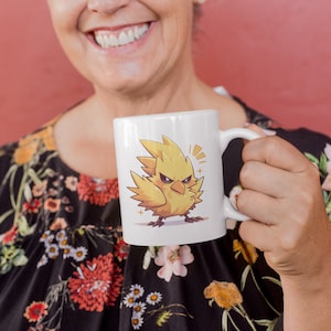 May include: A white ceramic mug with a yellow cartoon bird with a fierce expression. The bird has a yellow beak and black eyes. The mug has a black handle.