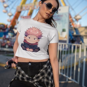 May include: A white crop top with a cartoon character printed on the front. The character is a young person with pink hair and is wearing a black and red outfit. The person is wearing black shorts and a plaid shirt tied around their waist.