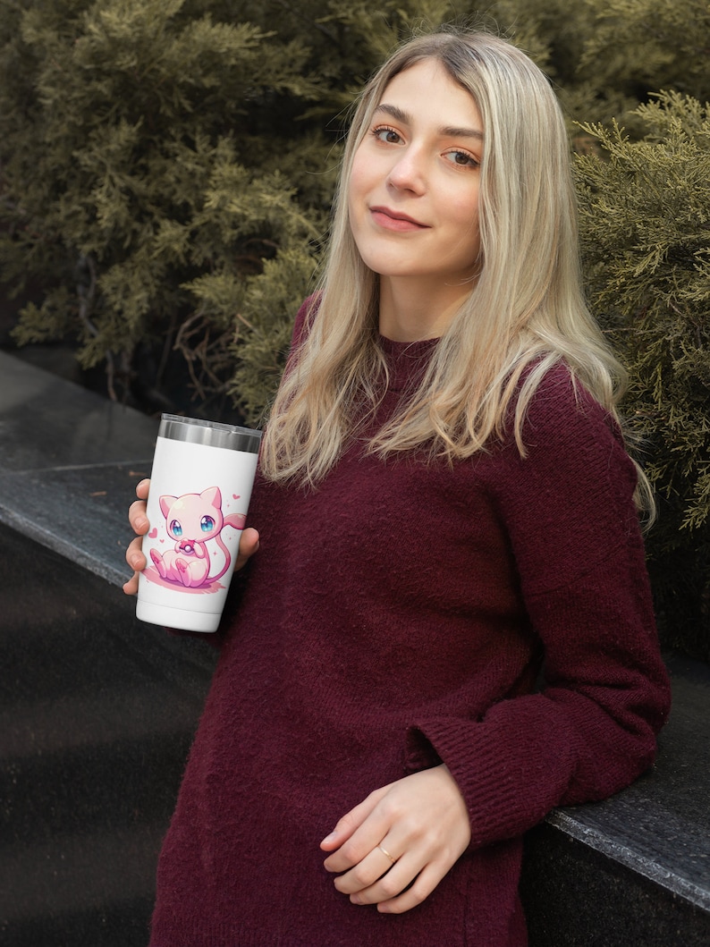May include: A white stainless steel travel mug with a pink cartoon cat holding a pink ball. The mug has a pink heart design around the cat.
