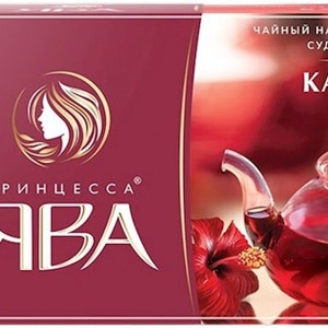May include: A box of Princess Java hibiscus tea bags. The box is red with gold lettering and a picture of a glass teapot filled with hibiscus tea. The text on the box reads "Чайный напиток из лепестков суданской розы Каркаде" which translates to "Tea drink from Sudanese rose petals Hibiscus".
