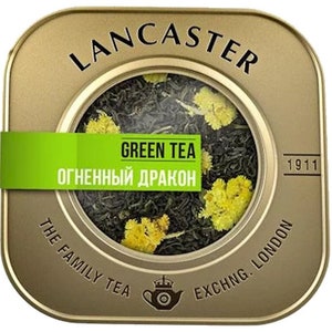 May include: A square, gold-colored tin of Lancaster Green Tea. The tin has a clear window showing green tea leaves and yellow flowers. A green label reads "GREEN TEA" and "ОГНЕННЫЙ ДРАКОН". The tin also has the text "THE FAMILY TEA EXCHNG. LONDON".