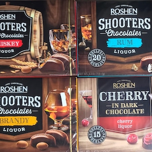 May include: Four boxes of Roshen Shooters chocolates. Each box features a different flavor: Whiskey, Brandy, Rum, and Cherry in Dark Chocolate. The boxes are decorated with images of the corresponding liquor and chocolates.
