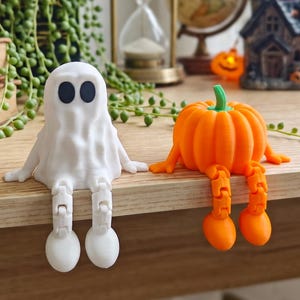 May include: A white ghost figurine and an orange pumpkin figurine, both featuring articulated dangling legs. The ghost has two black oval eyes, and the pumpkin has a green stem. These decorative figures are designed to sit on a flat edge.