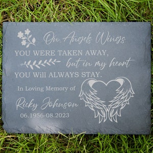 May include: A gray slate memorial plaque with the text "On Angels Wings You Were Taken Away, but in my heart You Will Always Stay."  It also includes the text "In Loving Memory of Ricky Johnson 06.1956-08.2023" and a heart with angel wings.