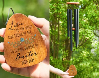 May include: A wooden wind chime with a brown wooden plaque that reads "Listen to the wind and think of me. In loving memory of Buster 2010-2024". The plaque has a floral design with blue flowers.