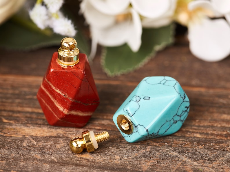 Op de afbeelding: Twee kleine, geometrisch gevormde flessen met gouden doppen. E&eacute;n fles is rood met witte strepen en de andere is blauw met witte aderen.
