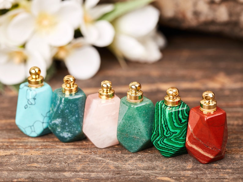 Op de afbeelding: Zes kleine, edelsteenvormige flesjes met gouden dopjes. De flesjes zijn gemaakt van turquoise, groen, roze, groen, groen en rood.