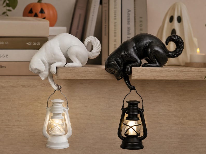 May include: Two dog figurines, one white and one black, are perched on a ledge. Each dog holds a small, lit lantern suspended from its front paw. The lanterns feature a classic design with a wire handle and a glowing light source inside the glass.