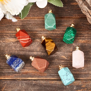 Op de afbeelding: Acht kleine edelsteenflesjes met gouden dopjes. De flesjes zijn gemaakt van verschillende stenen, waaronder rood, groen, bruin, blauw, roze en turquoise.