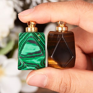 Op de afbeelding: Twee kleine, geometrisch gevormde flessen met gouden doppen. De fles aan de linkerkant is groen met zwarte strepen, en de fles aan de rechterkant is bruin met gouden strepen.