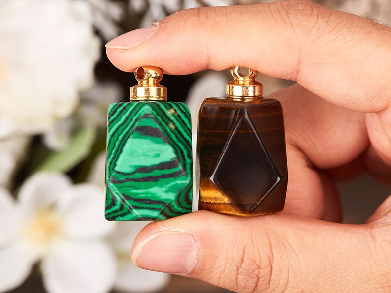 Op de afbeelding: Twee kleine, geometrisch gevormde flessen met gouden doppen. De fles aan de linkerkant is groen met zwarte strepen, en de fles aan de rechterkant is bruin met gouden strepen.