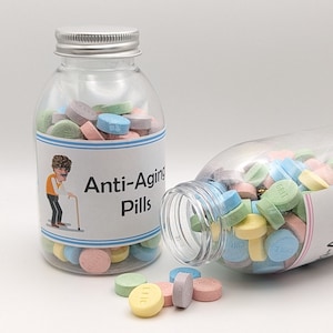 May include: Two clear plastic jars filled with colorful pastel candy. The jars have labels that say "Anti-Aging Pills". One jar is open and some of the candy is spilling out.