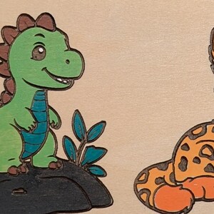 May include: Wooden puzzle featuring four cartoon animals: a deer, a dinosaur, a jaguar, and a penguin. The deer is brown with yellow accents, the dinosaur is green, the jaguar is orange with black spots, and the penguin is black and white.