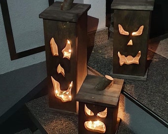 May include: Three wooden Halloween lanterns with carved jack-o'-lantern faces. Each lantern has a wooden top with a small branch attached. The lanterns are lit from within, creating a spooky glow. The lanterns are different sizes.