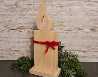 May include: A wooden candle-shaped decoration with a flame cutout at the top. The natural wood-colored candle is wrapped with a red yarn bow. Green pine branches are placed at the base of the candle, against a light wood-grain background.