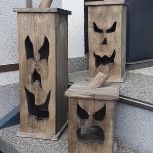 May include: Three wooden Halloween decorations shaped like jack-o'-lanterns. Each has a carved face with different expressions and a wooden stem. The wood has a natural, weathered finish, and the lanterns vary in size.