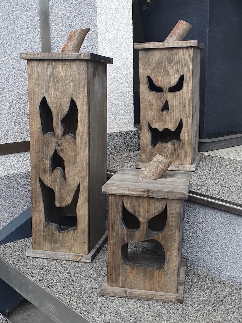 May include: Three wooden Halloween decorations shaped like jack-o'-lanterns. Each has a carved face with different expressions and a wooden stem. The wood has a natural, weathered finish, and the lanterns vary in size.
