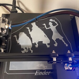 K&ouml;nnte beinhalten: Ein 3D-gedrucktes Modell von drei Figuren, einem Geist, einer Frau und einer Kreatur, auf einem schwarzen 3D-Druckbett. Das Modell ist in wei&szlig;em Filament gedruckt. Der Drucker ist mit "Ender" beschriftet.