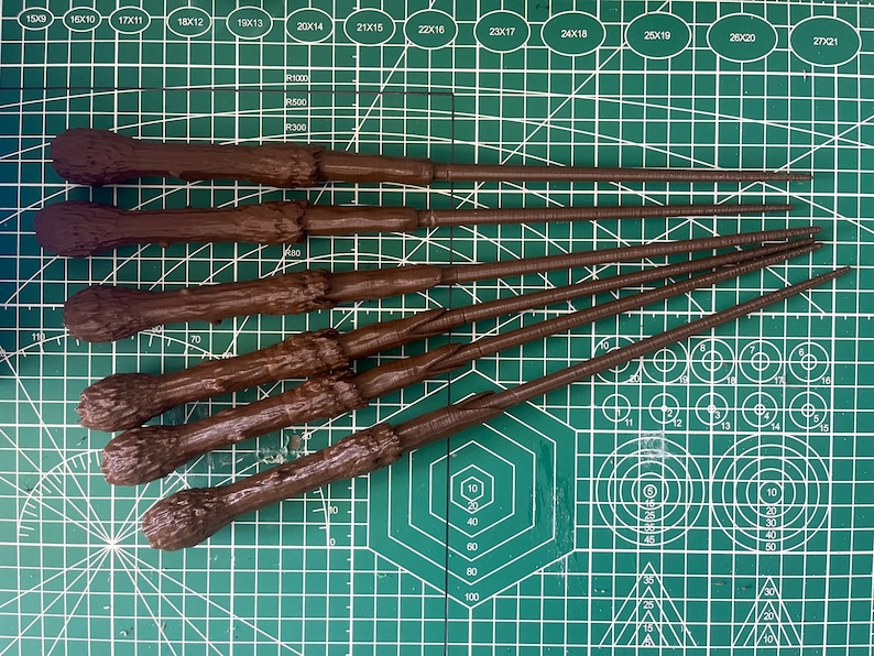 K&ouml;nnte beinhalten: F&uuml;nf braune Holzst&auml;be mit strukturierter Oberfl&auml;che, angeordnet auf einer gr&uuml;nen Schneidematte mit wei&szlig;en Markierungen.