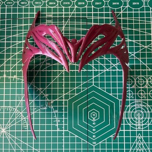 K&ouml;nnte beinhalten: Ein rotes Plastik-Haarband mit einem detaillierten, komplizierten Design. Das Haarband ist aus flexiblem Material und hat eine gebogene Form.