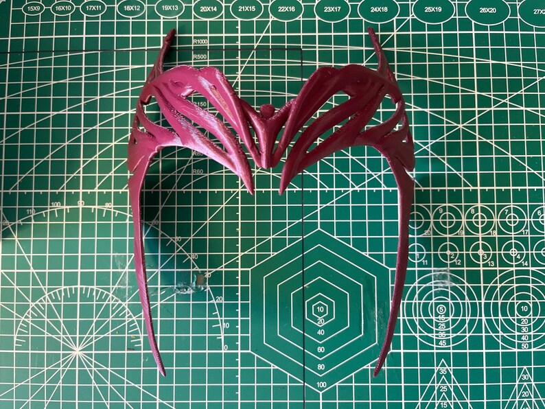 K&ouml;nnte beinhalten: Ein rotes Plastik-Haarband mit einem detaillierten, komplizierten Design. Das Haarband ist aus flexiblem Material und hat eine gebogene Form.