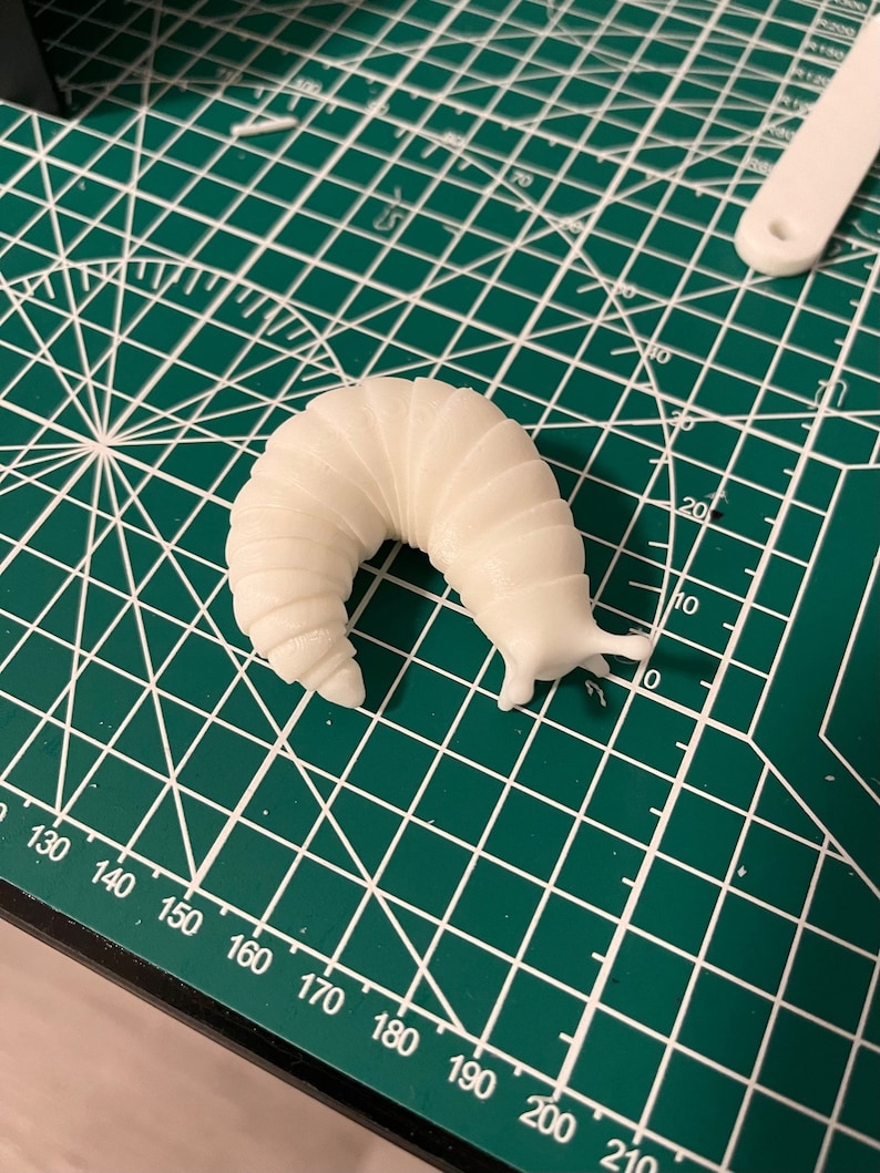K&ouml;nnte beinhalten: Ein wei&szlig;es 3D-gedrucktes Modell einer Schnecke auf einer gr&uuml;nen Schneidematte.