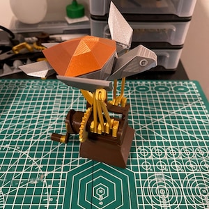 K&ouml;nnte beinhalten: Eine 3D-gedruckte Steampunk-Schildkr&ouml;te mit brauner Schale, silbernen Beinen und goldenen Zahnr&auml;dern. Die Schildkr&ouml;te ist auf einem Holzsockel mit einer Kurbel montiert.