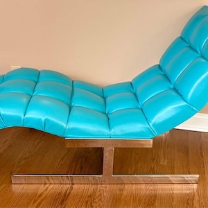 May include: A modern chaise lounge in a vibrant turquoise color. The seat is tufted and curved, supported by a polished metal base. The lounge is designed for relaxation and adds a pop of color to any living space.