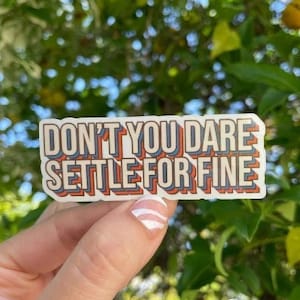 May include: A white sticker with the text "Don't you dare settle for fine" in red, blue, and yellow letters. The sticker has a retro, layered design.